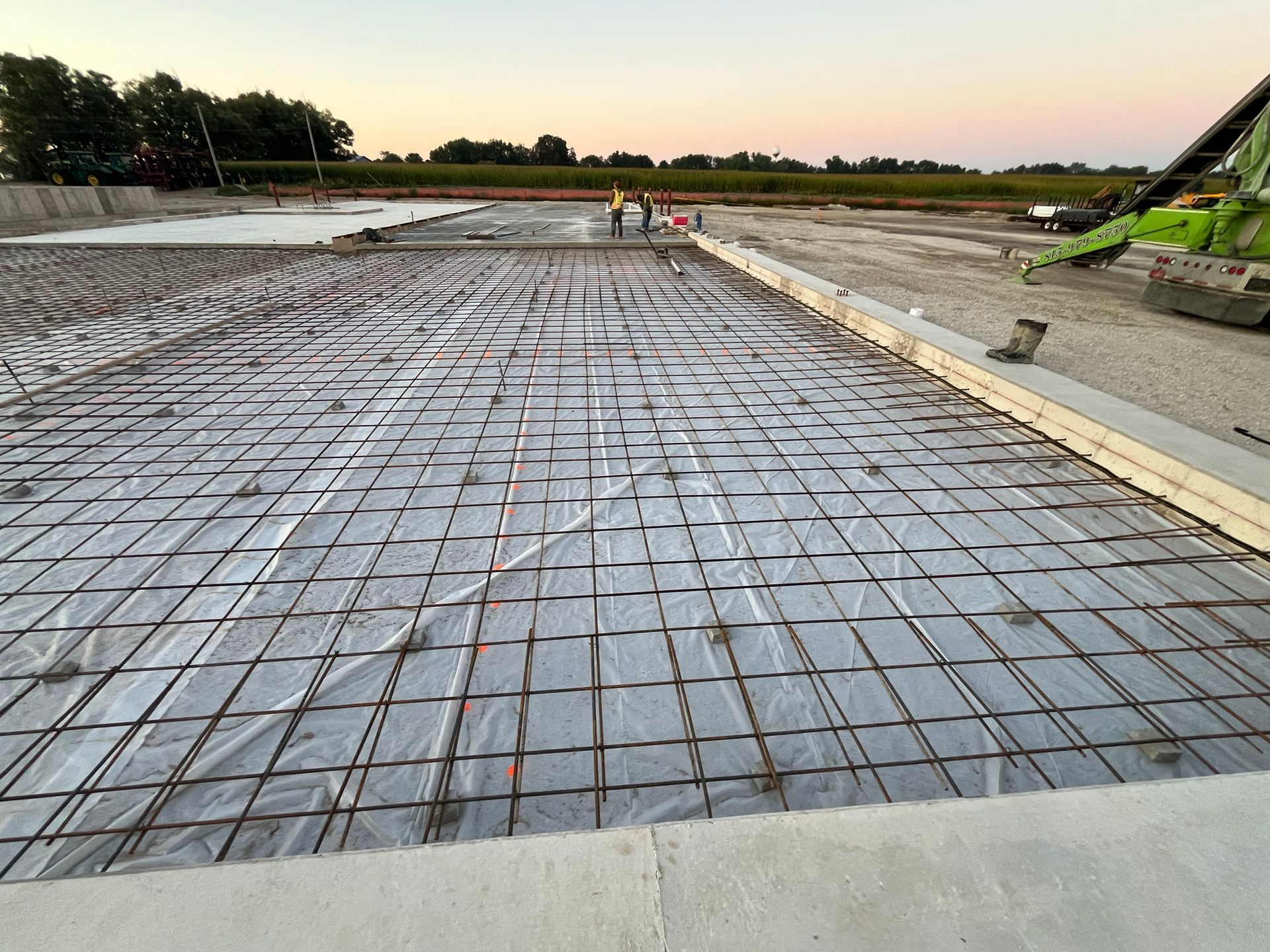 Construction site with rebar grid covered by plastic sheeting, ready for concrete pouring.