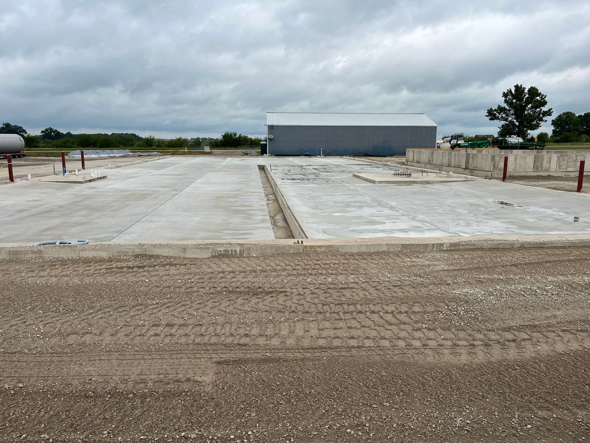 Concrete foundation with a gravel foreground, a metal building in the distance, and an overcast sky.