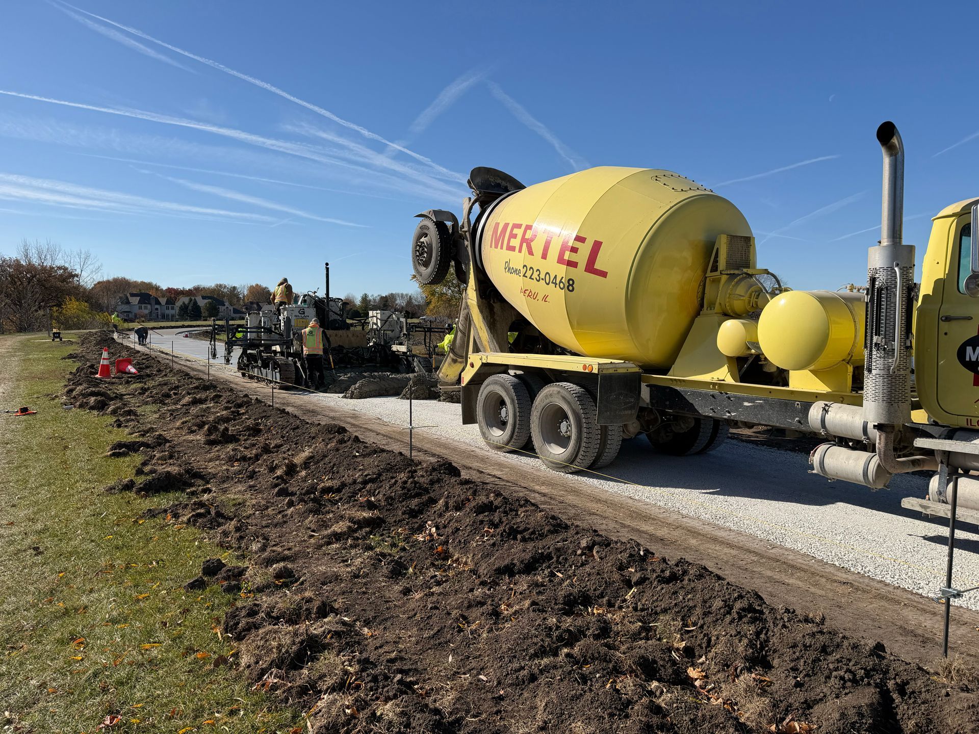 Concrete truck pouring cement on a gravel path next to a grassy area, outdoors.