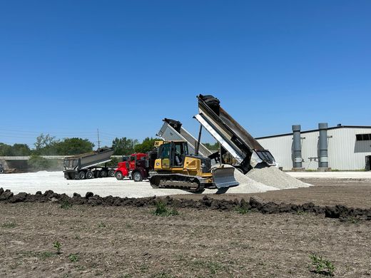 Construction site: Yellow excavator loading gravel into a red dump truck, blue sky.