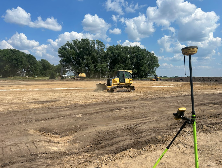 Construction site with bulldozer, GPS equipment, and cloudy blue sky.