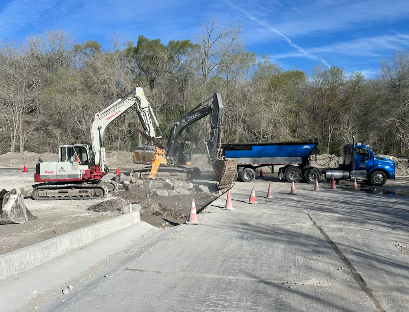 Construction scene: excavators breaking up pavement, truck waiting to receive debris.
