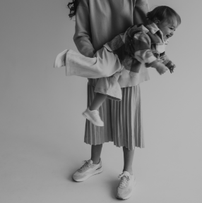 Adult carrying a smiling child in a grayscale studio portrait, both wearing casual clothes and sneakers
