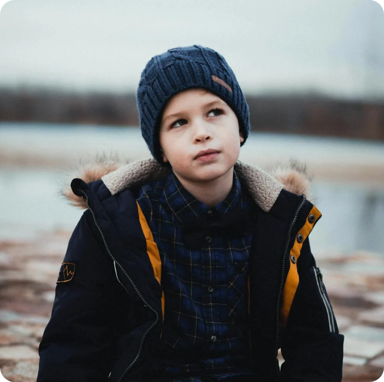 Child in a navy knit hat and winter coat looking off-camera outdoors by a blurred lakeshore