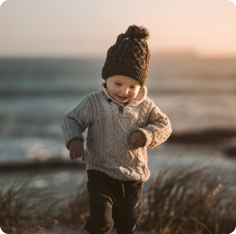 Toddler in a knit hat and sweater walking outdoors at sunset with a blurred field behind them