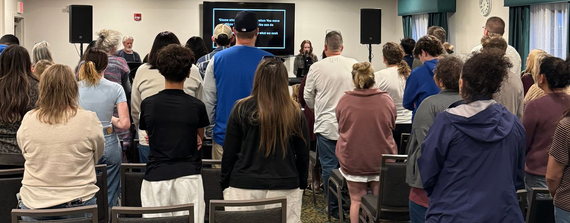 People standing and facing a stage in a conference room, listening to a presentation