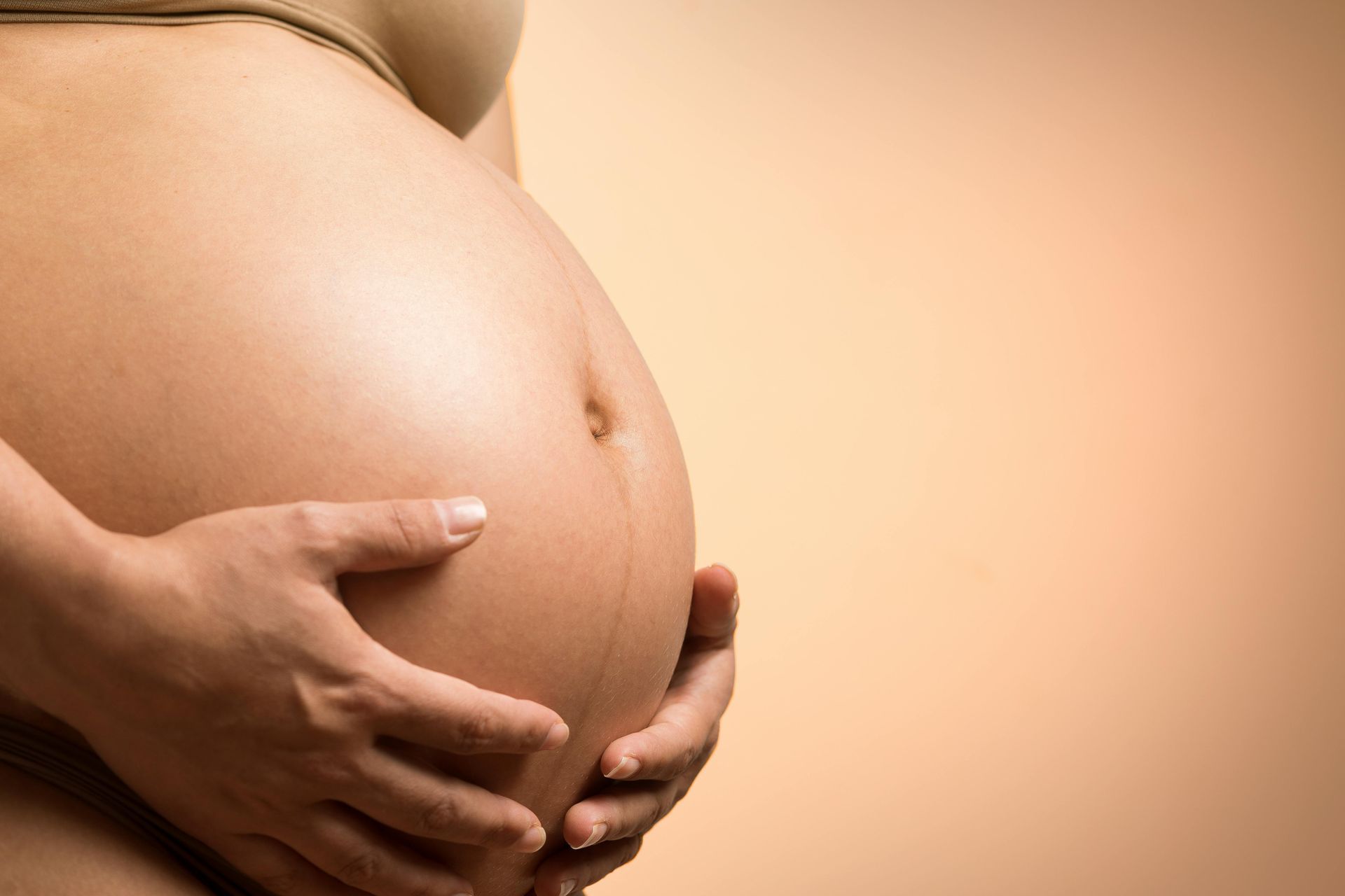 Pregnant belly with hands resting on abdomen against a warm beige background