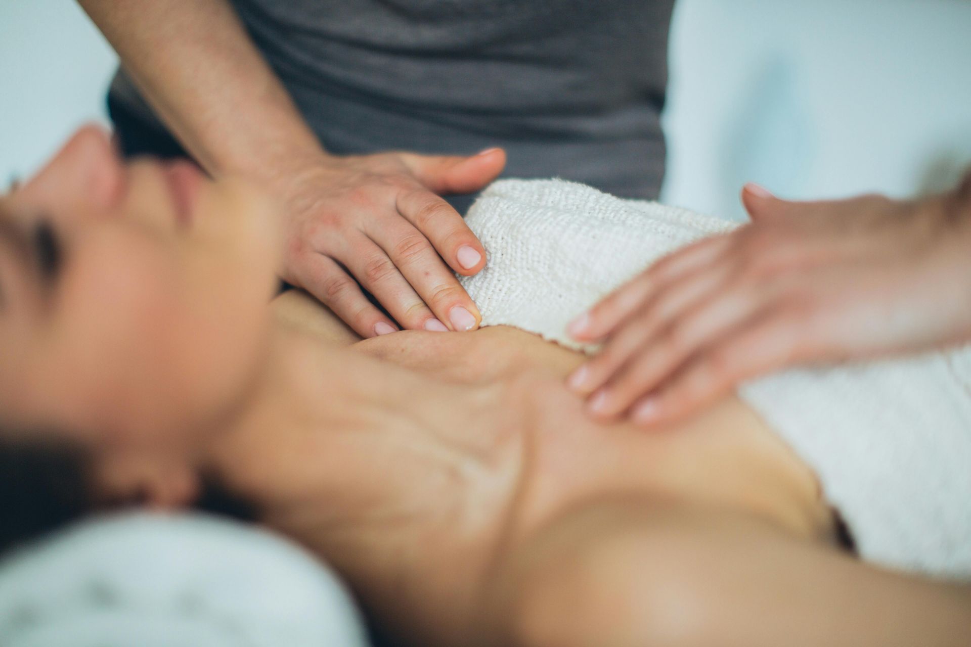 Two hands gently massaging a person’s bare back on a white towel.