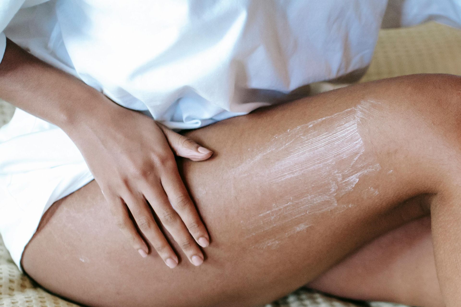 Hand applying lotion to a bare leg on a white towel