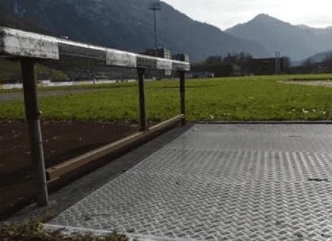 Eine Person springt über eine Hürde auf einem Feld mit Bergen im Hintergrund.