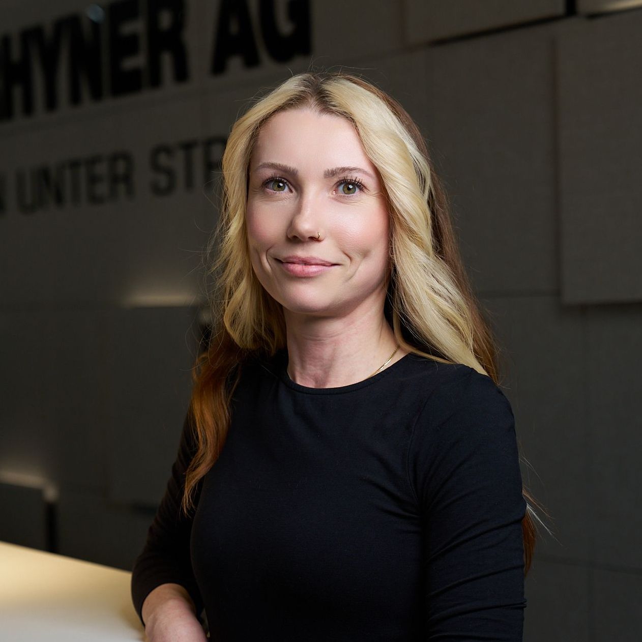Eine Frau in einem schwarzen Hemd steht vor einem Schild mit der Aufschrift „Elektro Rhyner AG“