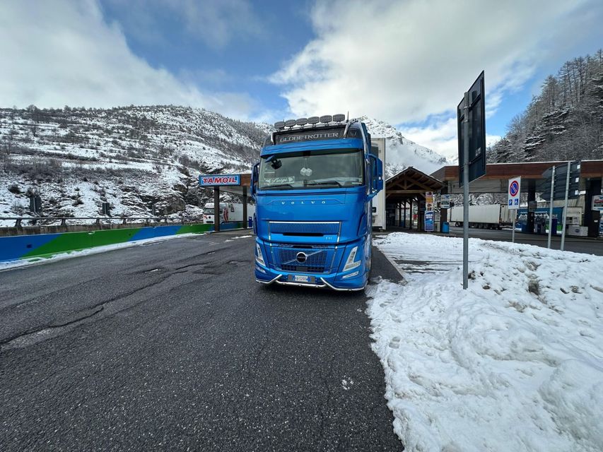 Un camioncino blu parcheggiato sul ciglio di una strada innevata in un paesaggio montano invernale.
