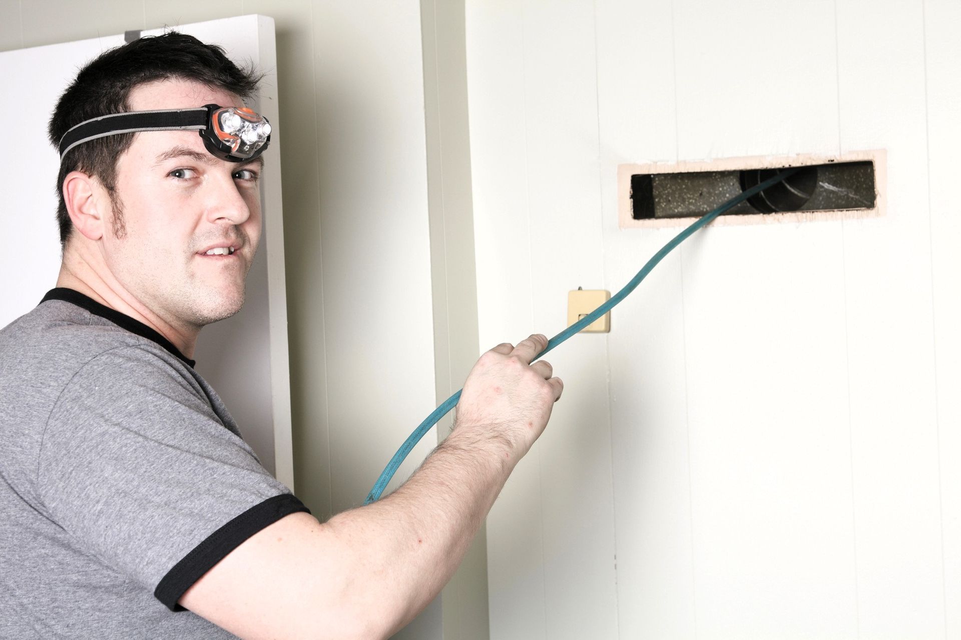 Person cleaning hard-to-reach duct with a hose and headlamp