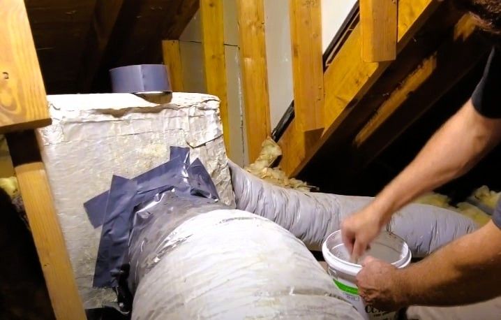 Technician performing emergency duct repair in attic sealing ductwork with tape and sealant