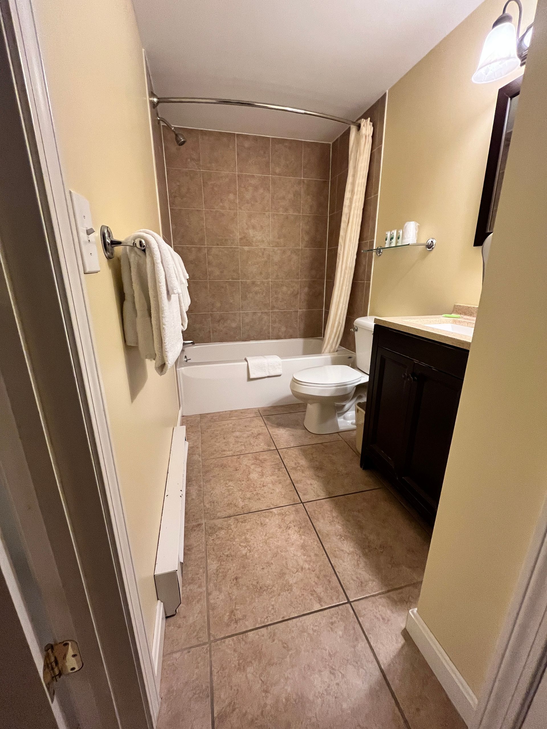Bathroom with brown tile shower, toilet, dark vanity, and tan walls. White towels on a rack.