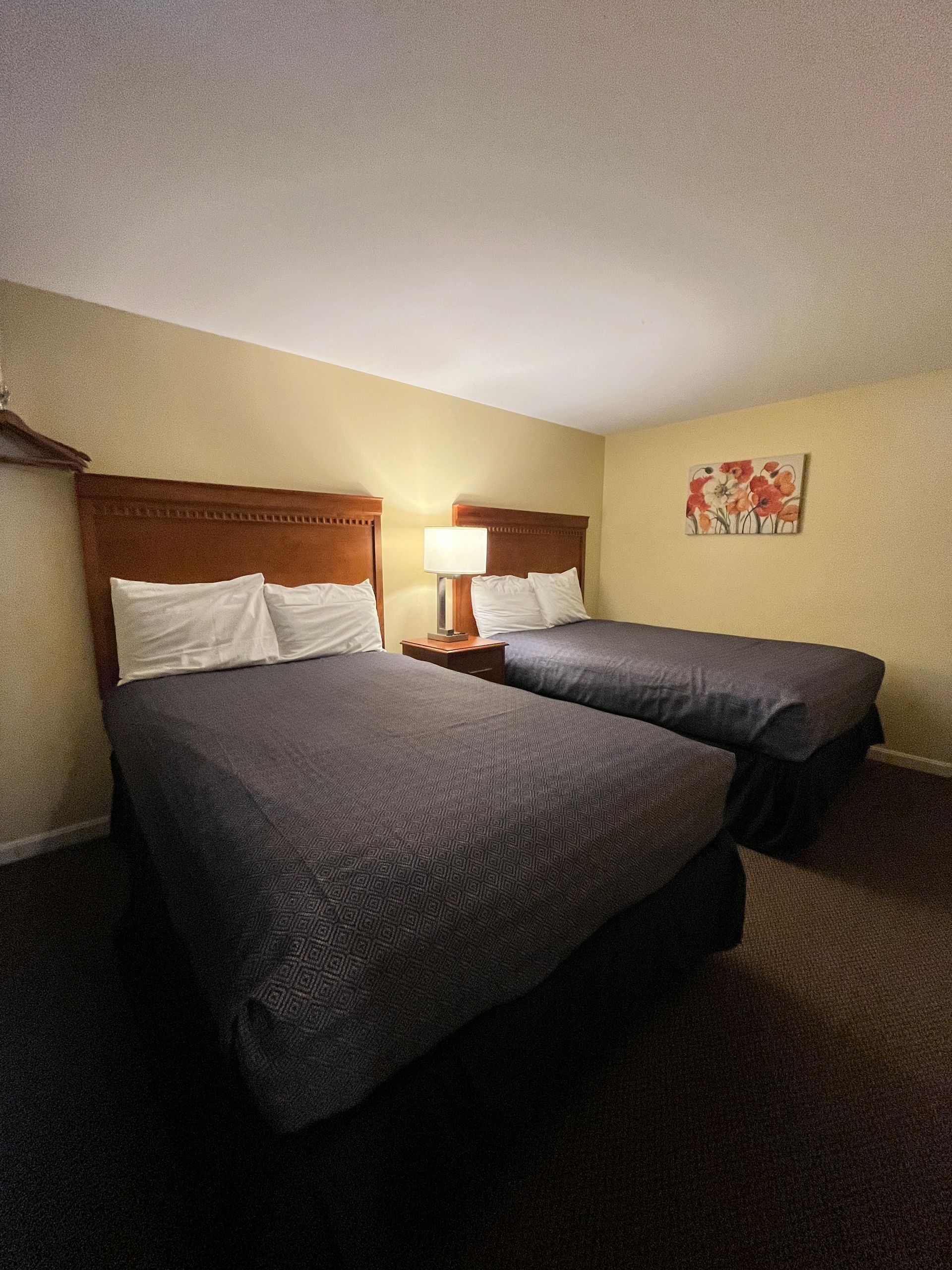 Hotel room with two beds, a nightstand with a lamp, and a floral painting on the wall.