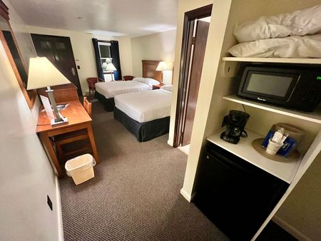 A hotel room with two beds , a desk , a microwave and a coffee maker.
