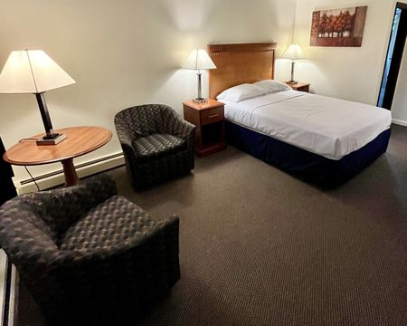 A hotel room with a bed and two chairs