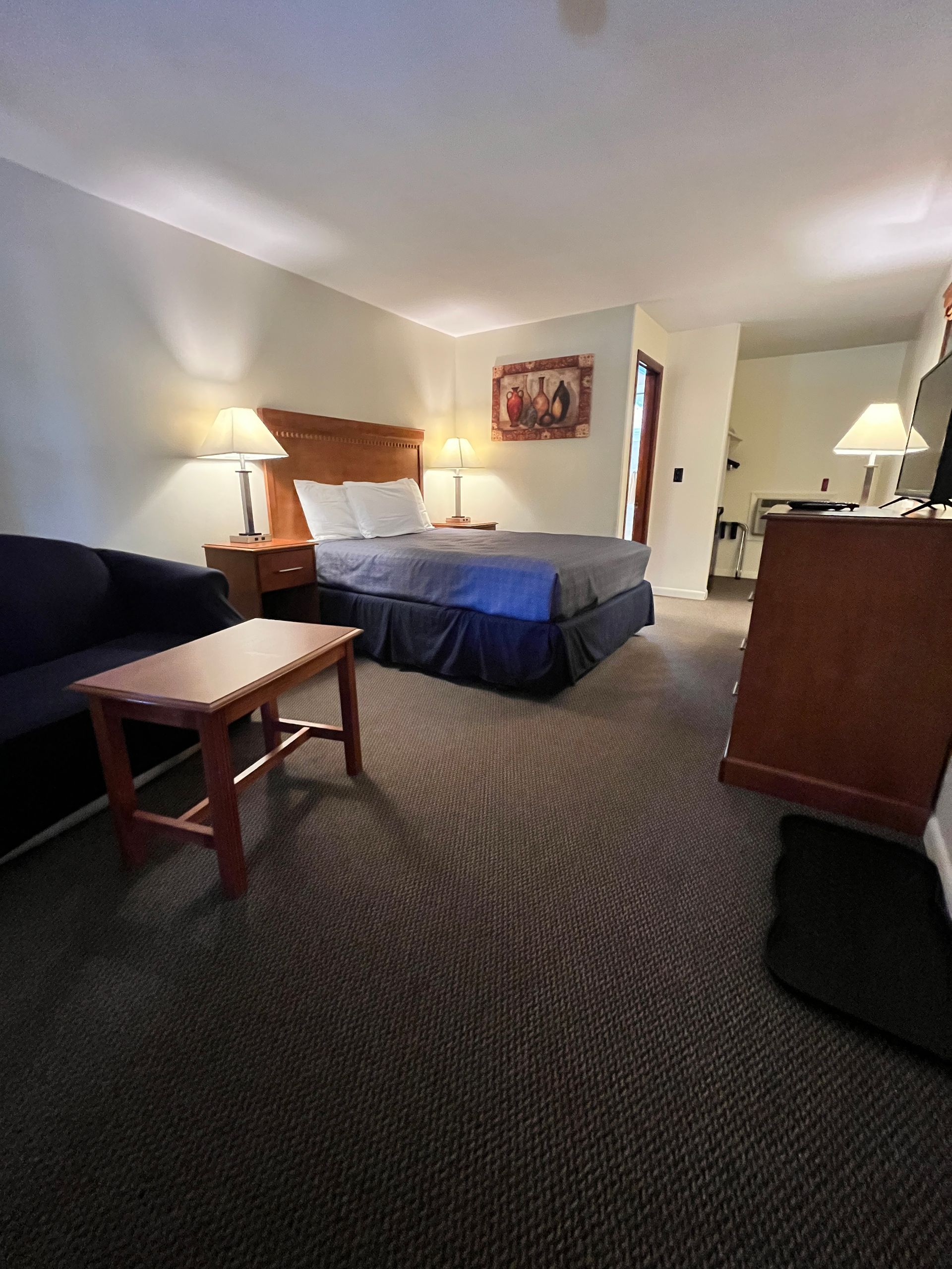 Hotel room with a bed, small sofa, coffee table, lamps, and a doorway.