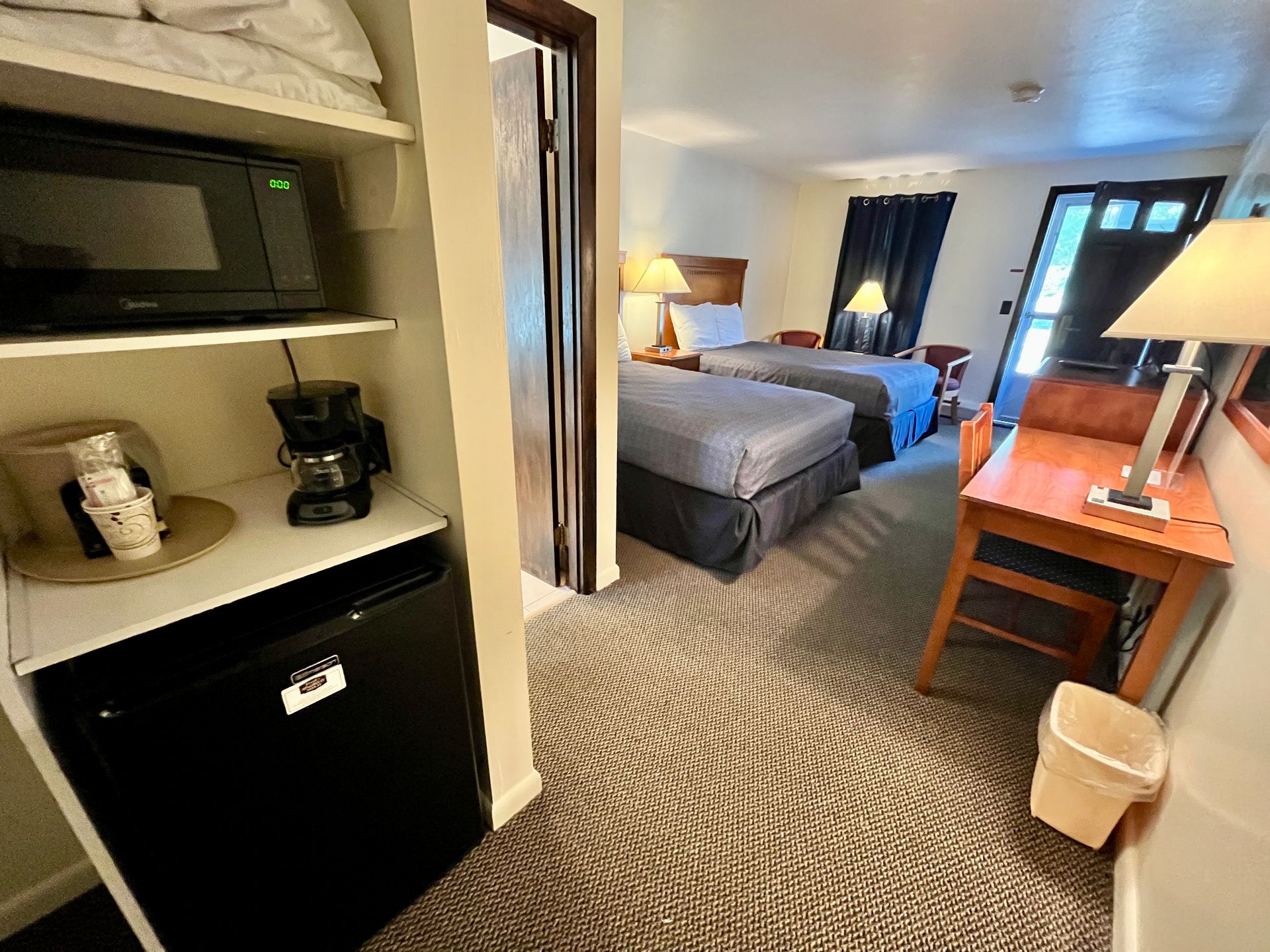 Hotel room with two beds, microwave, coffee maker, mini fridge, desk, and doorway to a bathroom.