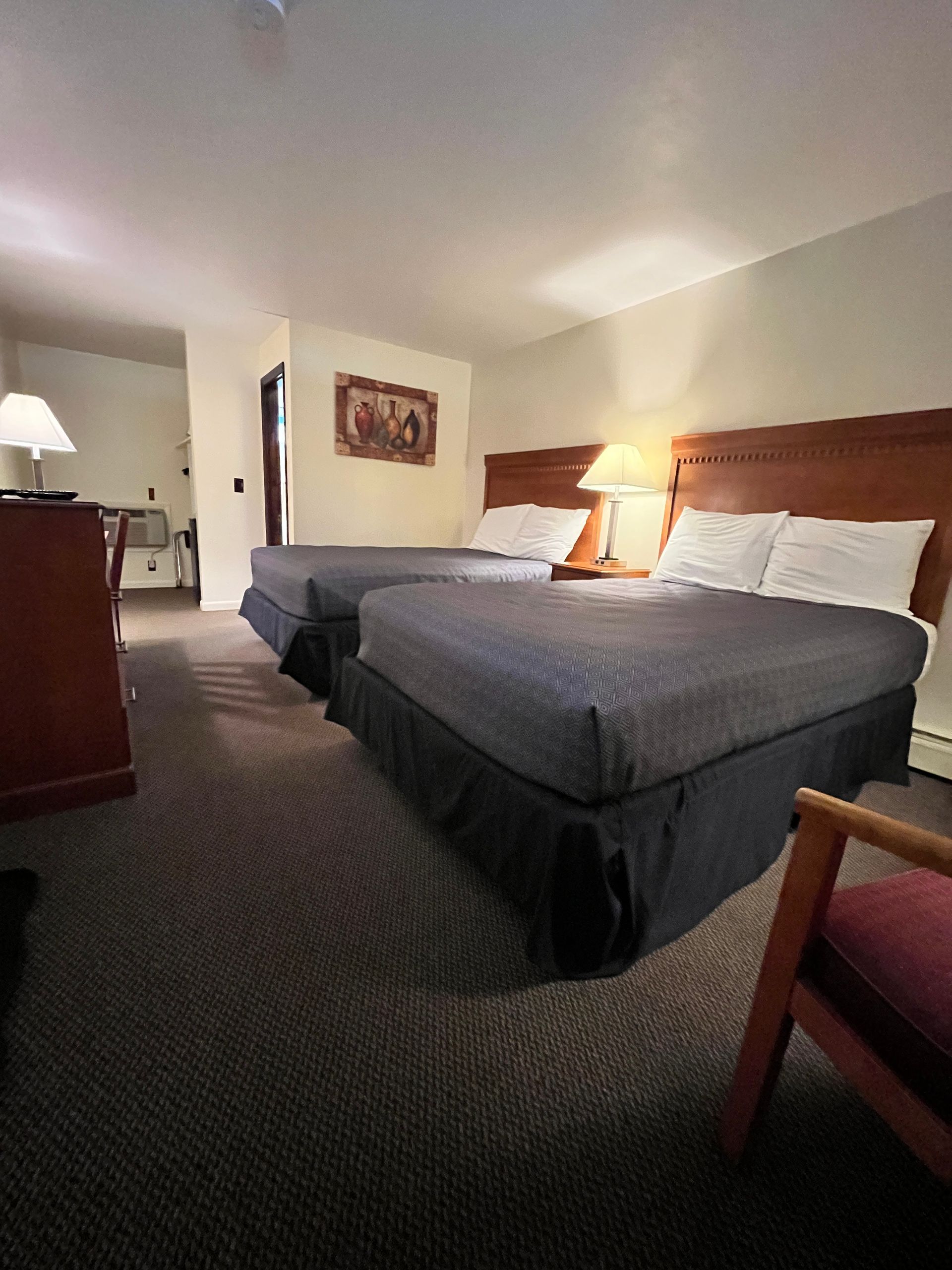 Bedroom with two queen beds, lamps, dark carpet, and a framed picture on the wall.