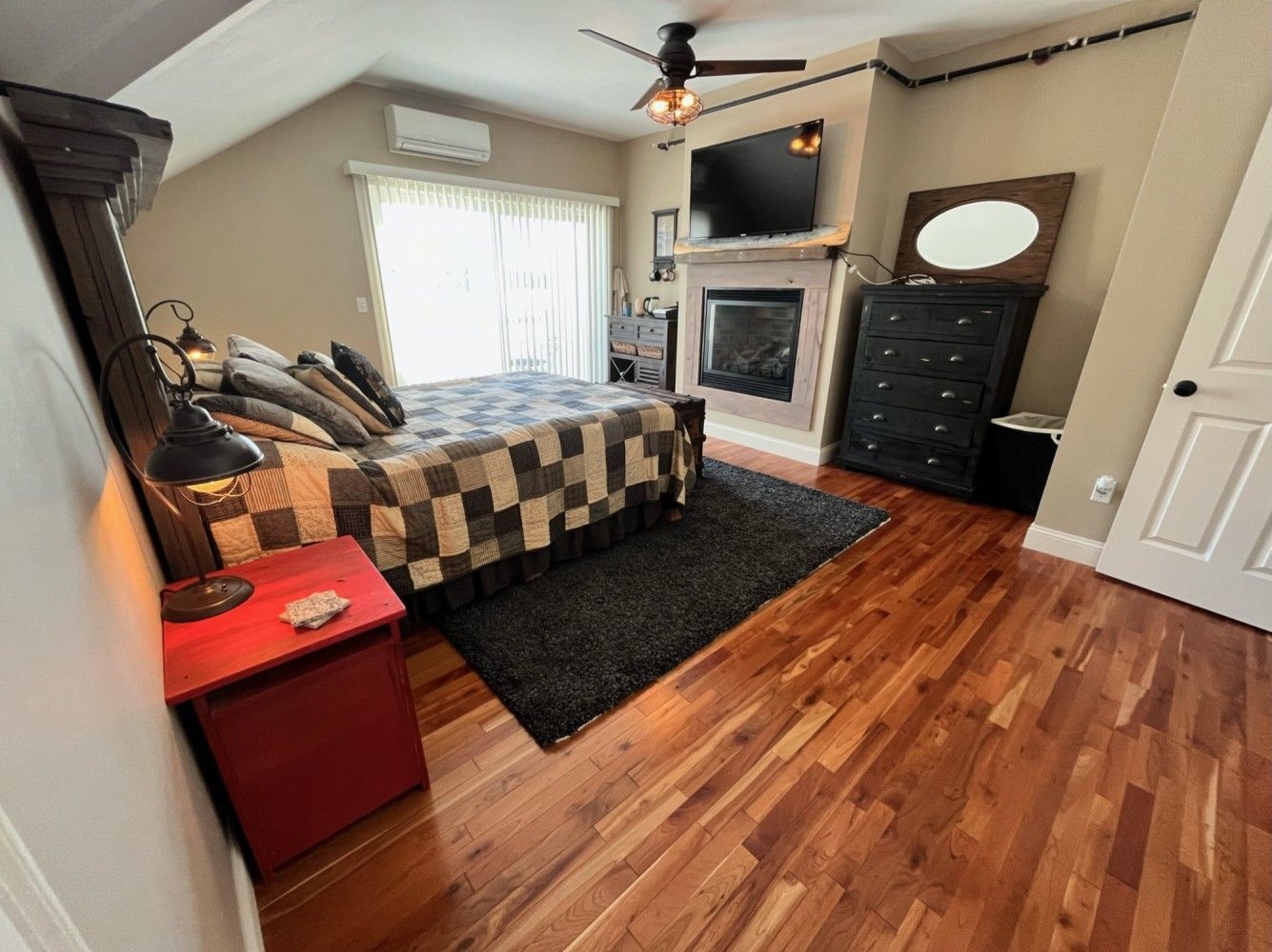 A bedroom with a bed , dresser , television and fireplace.