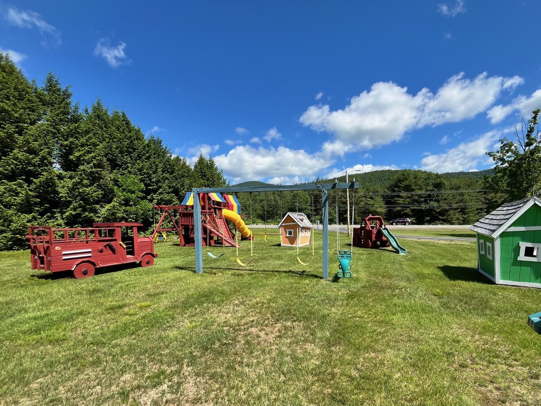 A playground with a fire truck , swings , and a green house.
