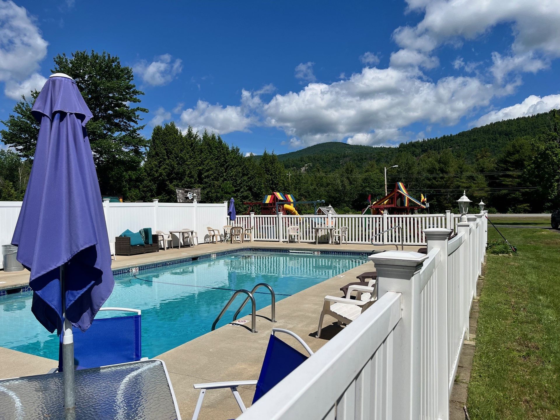 A swimming pool with a white fence and a purple umbrella