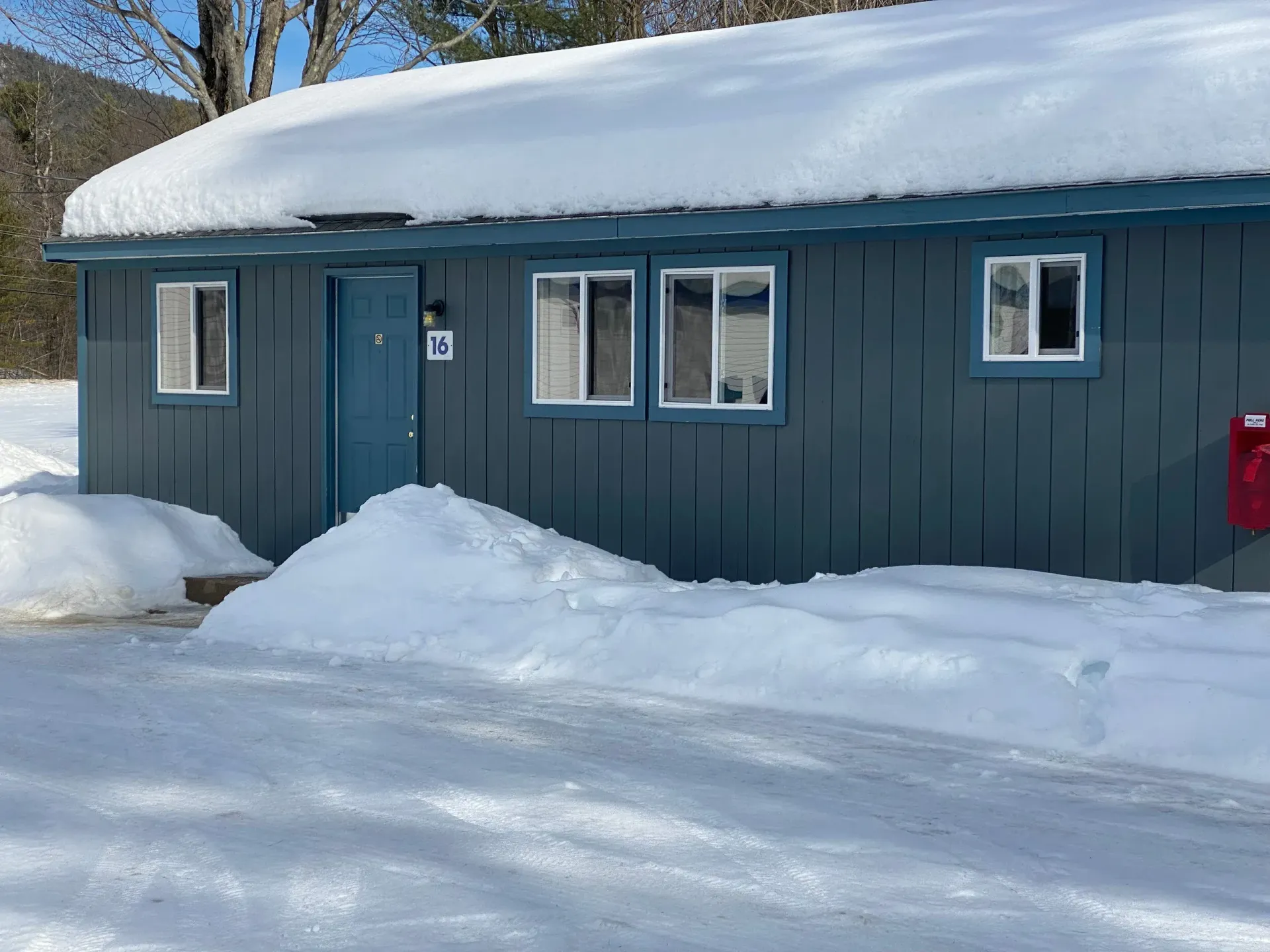 A blue house covered in snow with a red mailbox in front of it.
