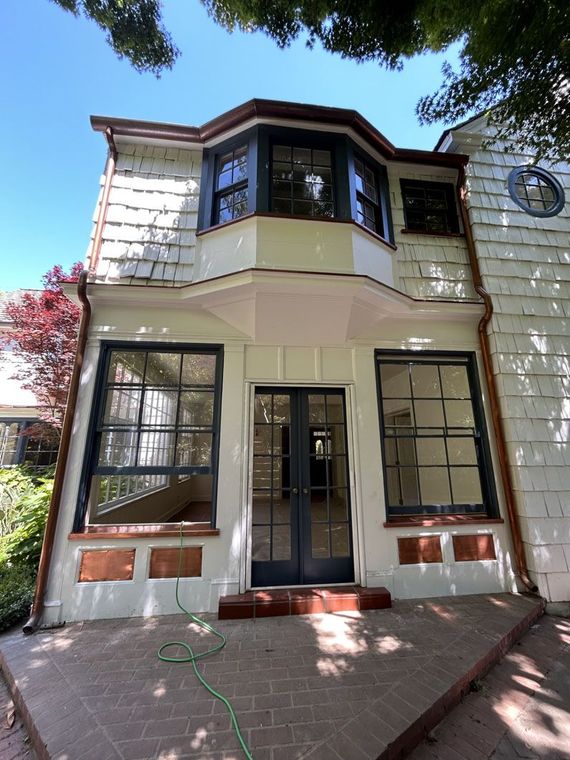 Two-story beige house with bay windows, a front door, and a brick walkway under a blue sky