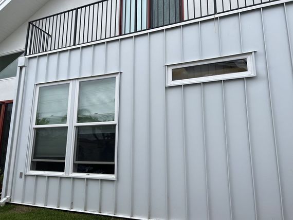 White metal-sided building exterior with a window and narrow horizontal vent above it.