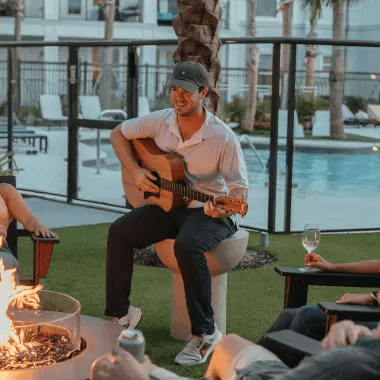 A man is sitting at a fire pit playing a guitar.