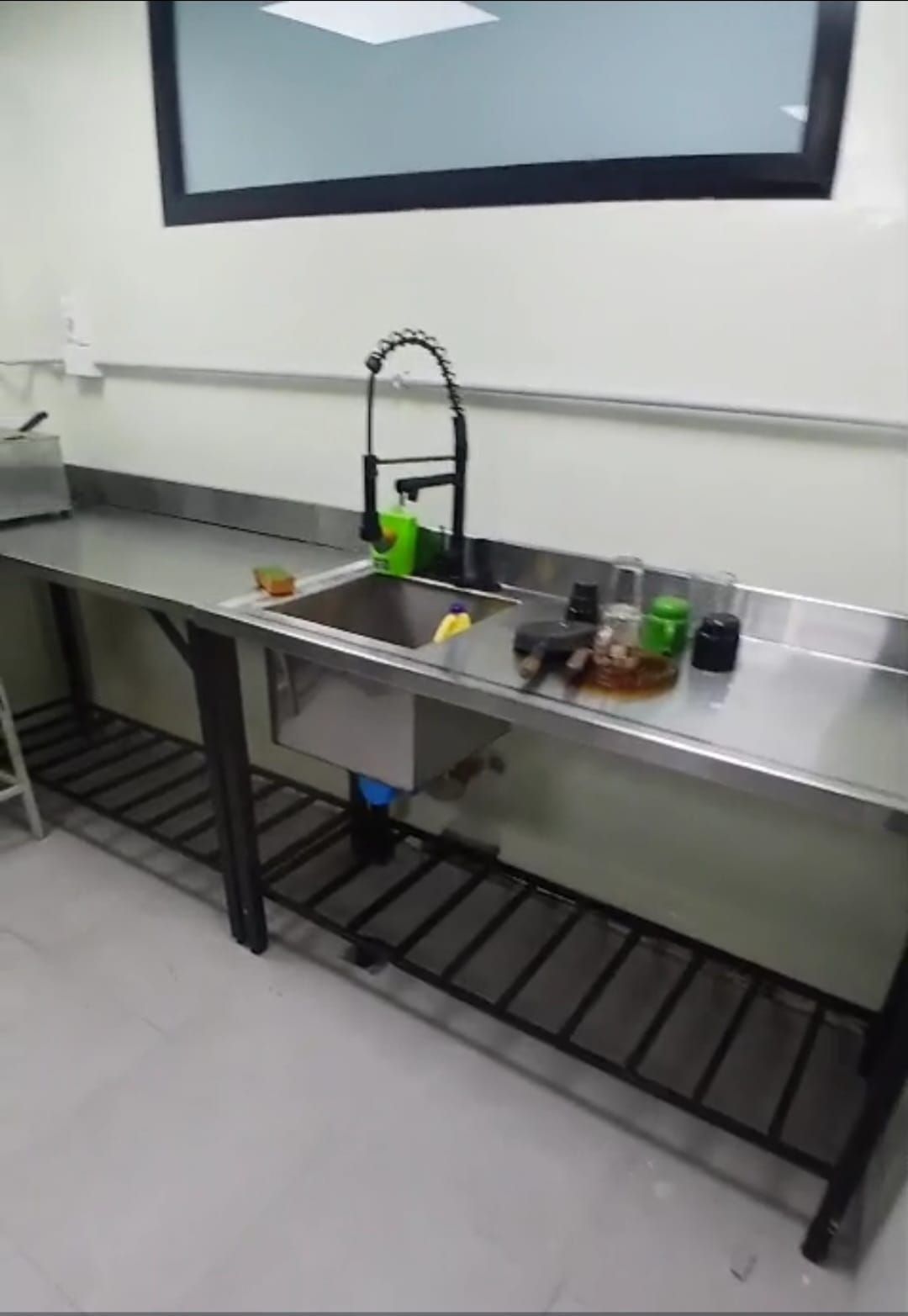 Fregadero y encimera de acero inoxidable con platos y utensilios en un espacio de trabajo de cocina o laboratorio.