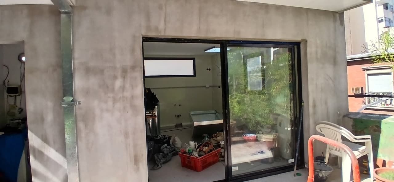 Edificio de hormigón con una gran puerta corredera de cristal y un taller interior parcialmente visible.