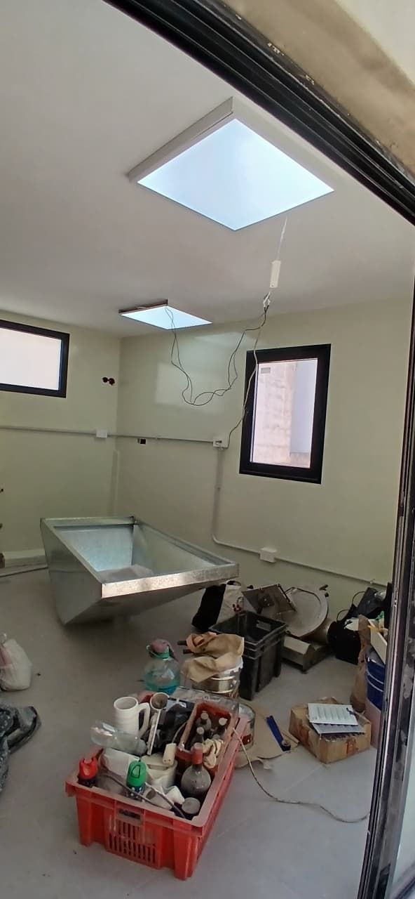 Baño sin terminar con tragaluz, ventanas, inodoro y herramientas amontonadas en el suelo.