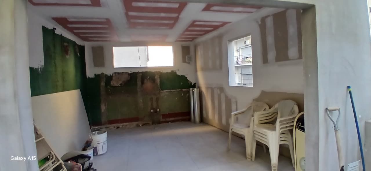 Habitación vacía con paredes verdes y beige, suelo blanco y sillas de plástico apiladas junto a una ventana.