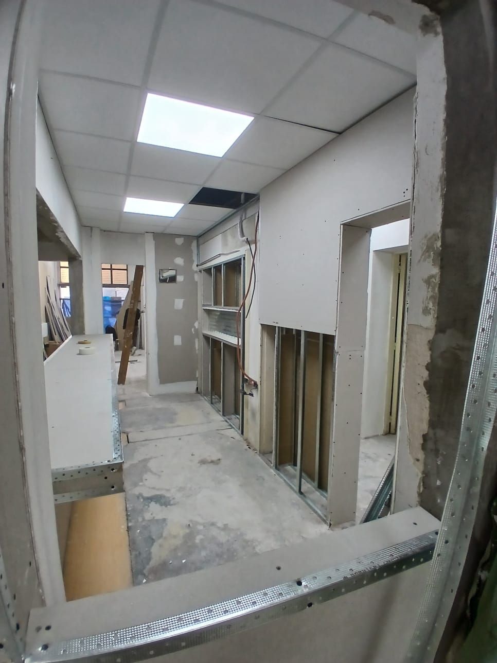 Pasillo estrecho sin terminar con estructura de madera a la vista, paneles de yeso y luces de techo en proceso de renovación.