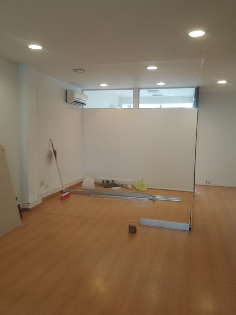 Habitación vacía con suelo de madera, paredes blancas, luces de techo y productos de limpieza cerca de la pared del fondo.