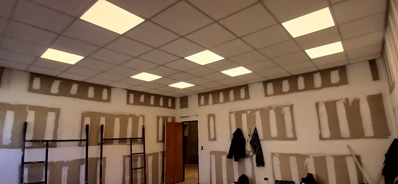 Habitación vacía en construcción con paredes sin terminar, luces de techo, escaleras y abrigos colgados cerca de una puerta.