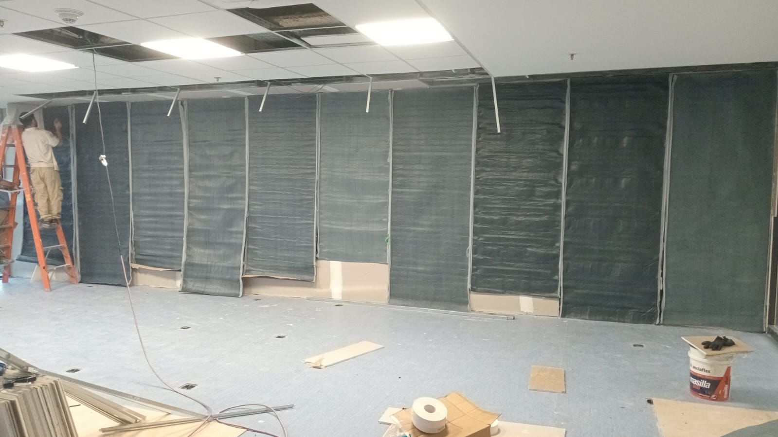 Interior de oficina en construcción con techo a la vista, paneles de pared negros y escombros en el suelo.