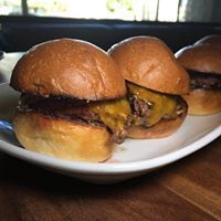 Three hamburgers are on a white plate on a wooden table.
