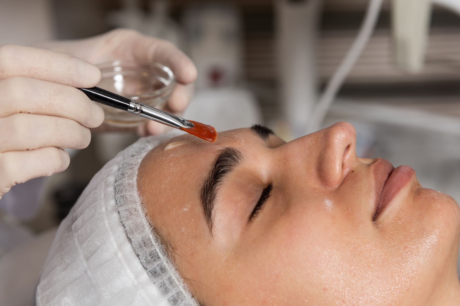 Esthetician applying serum to a woman’s forehead with a dropper during a facial treatment