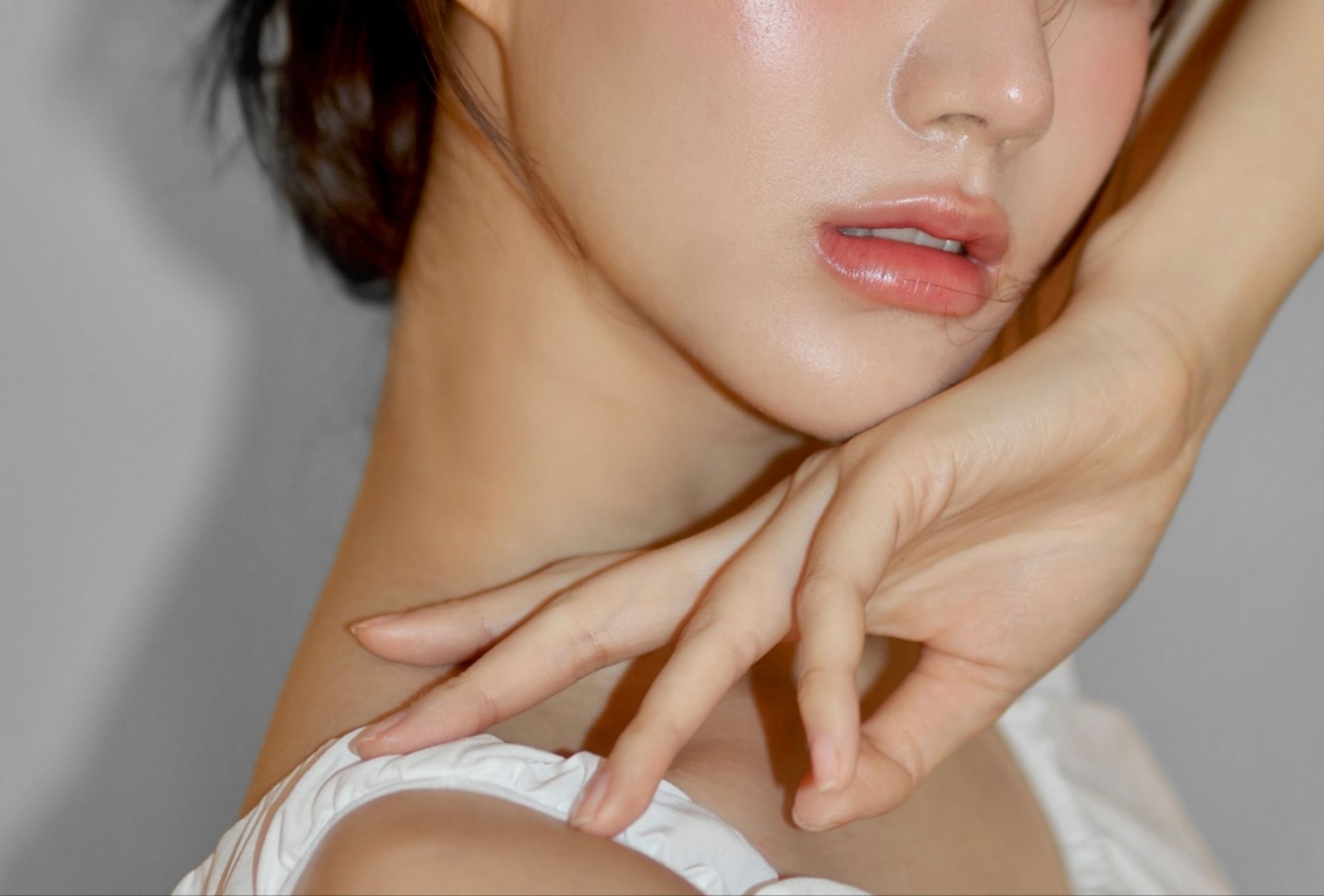 Close-up of a person posing with one hand near their neck, wearing a white top against a plain background