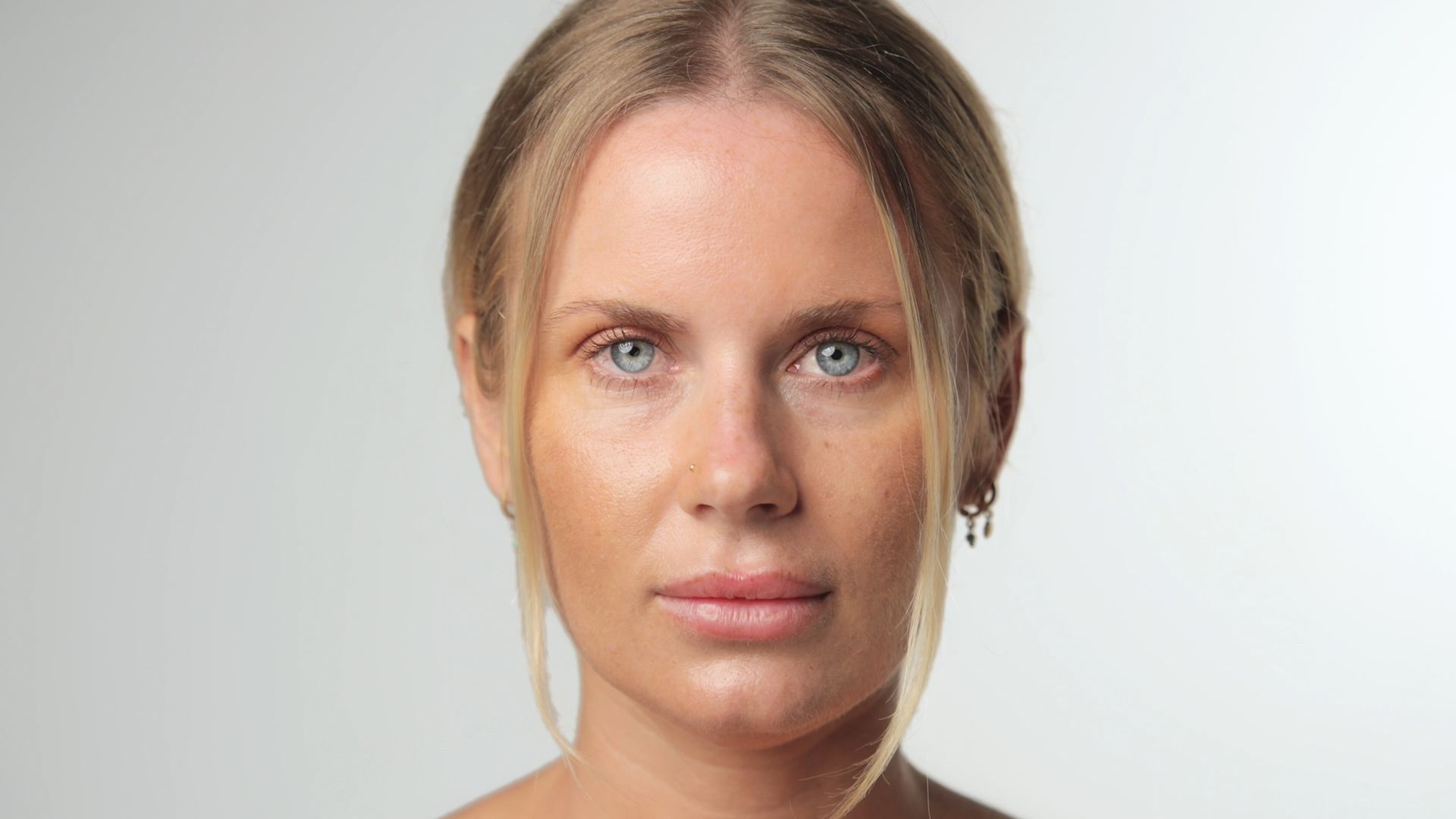Close-up portrait of a person with blonde hair, blue eyes, and a neutral expression on a light background