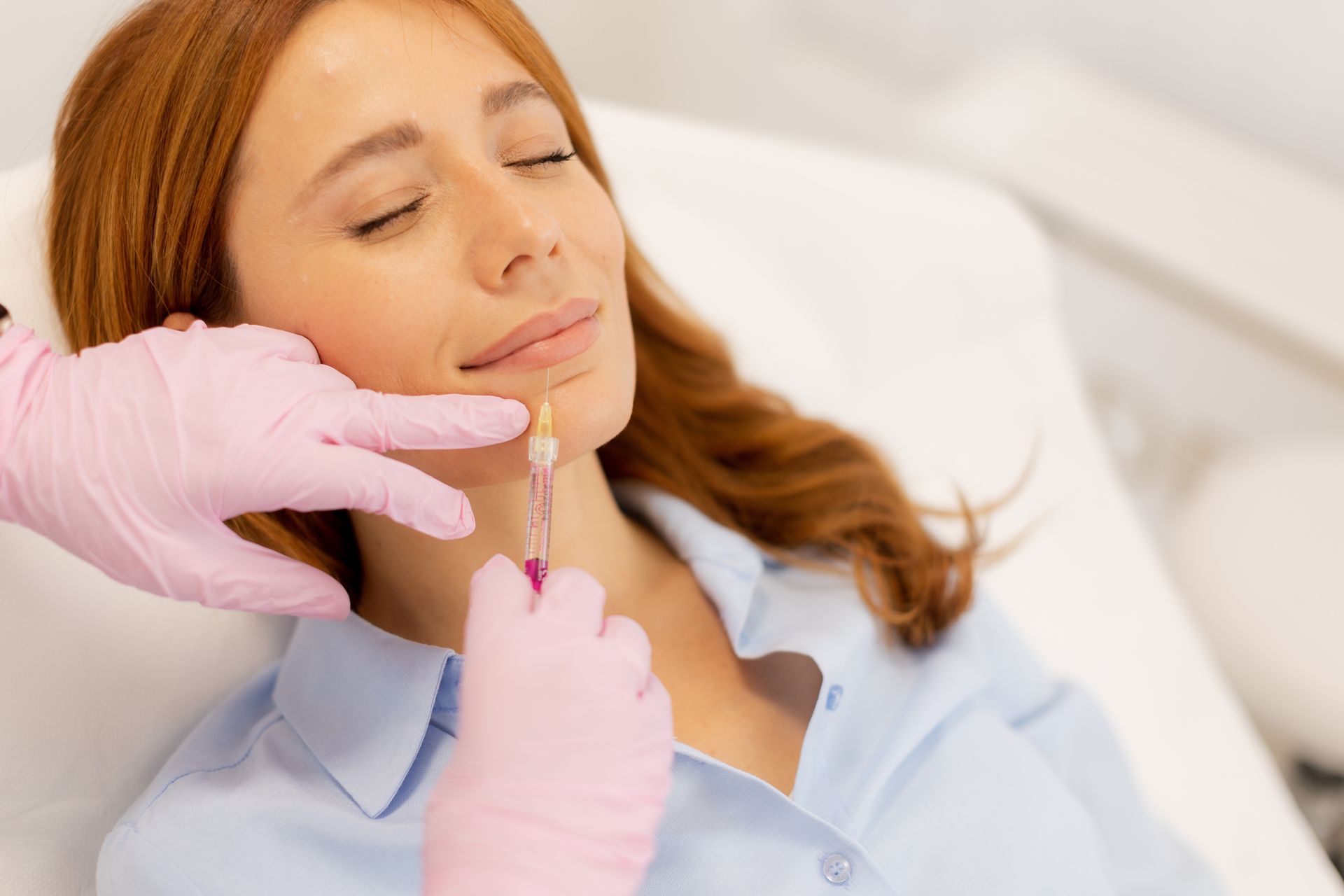Gloved practitioner injecting filler into a relaxed patient’s chin in a clinic setting