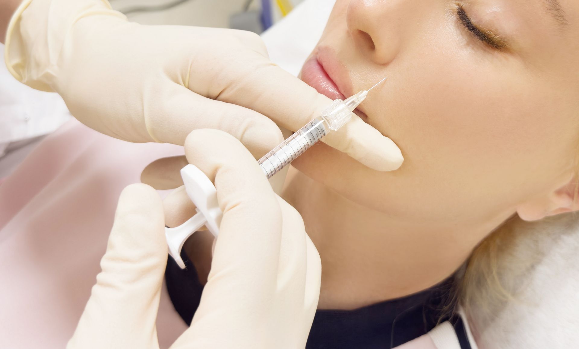 Gloved hands inject filler into a woman’s cheek with a syringe during a cosmetic procedure