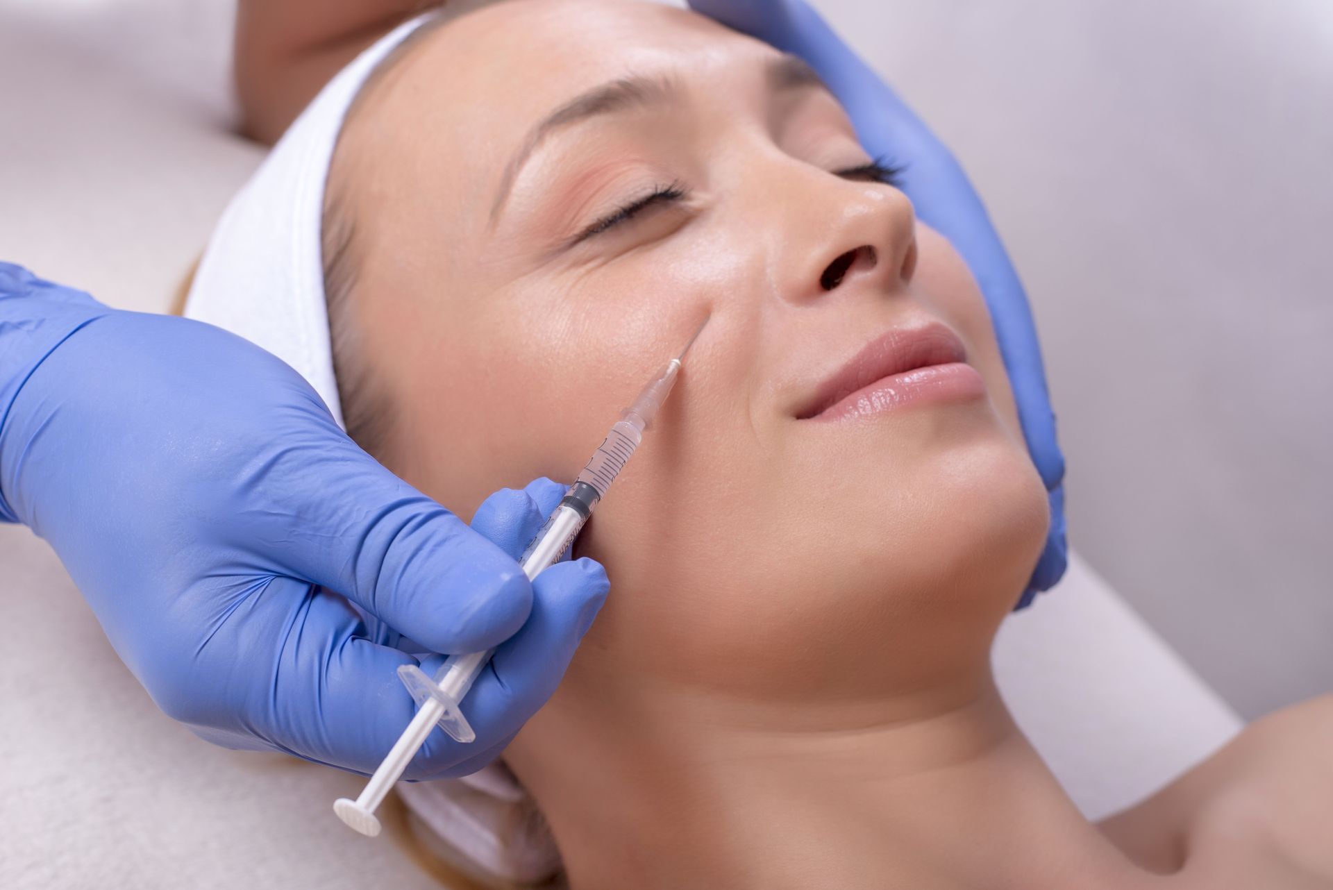 Gloved hands injecting filler into a woman’s cheek during a cosmetic procedure
