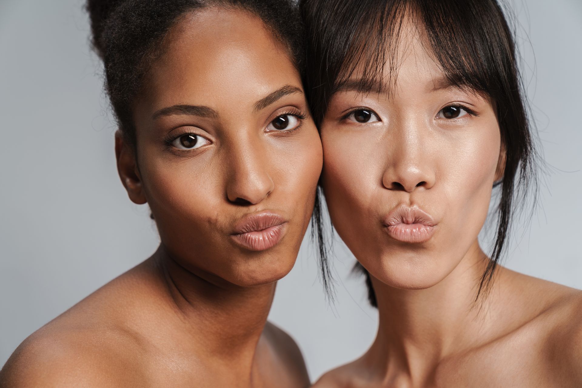 Two women posed closely together, making puckered lips against a light gray background.