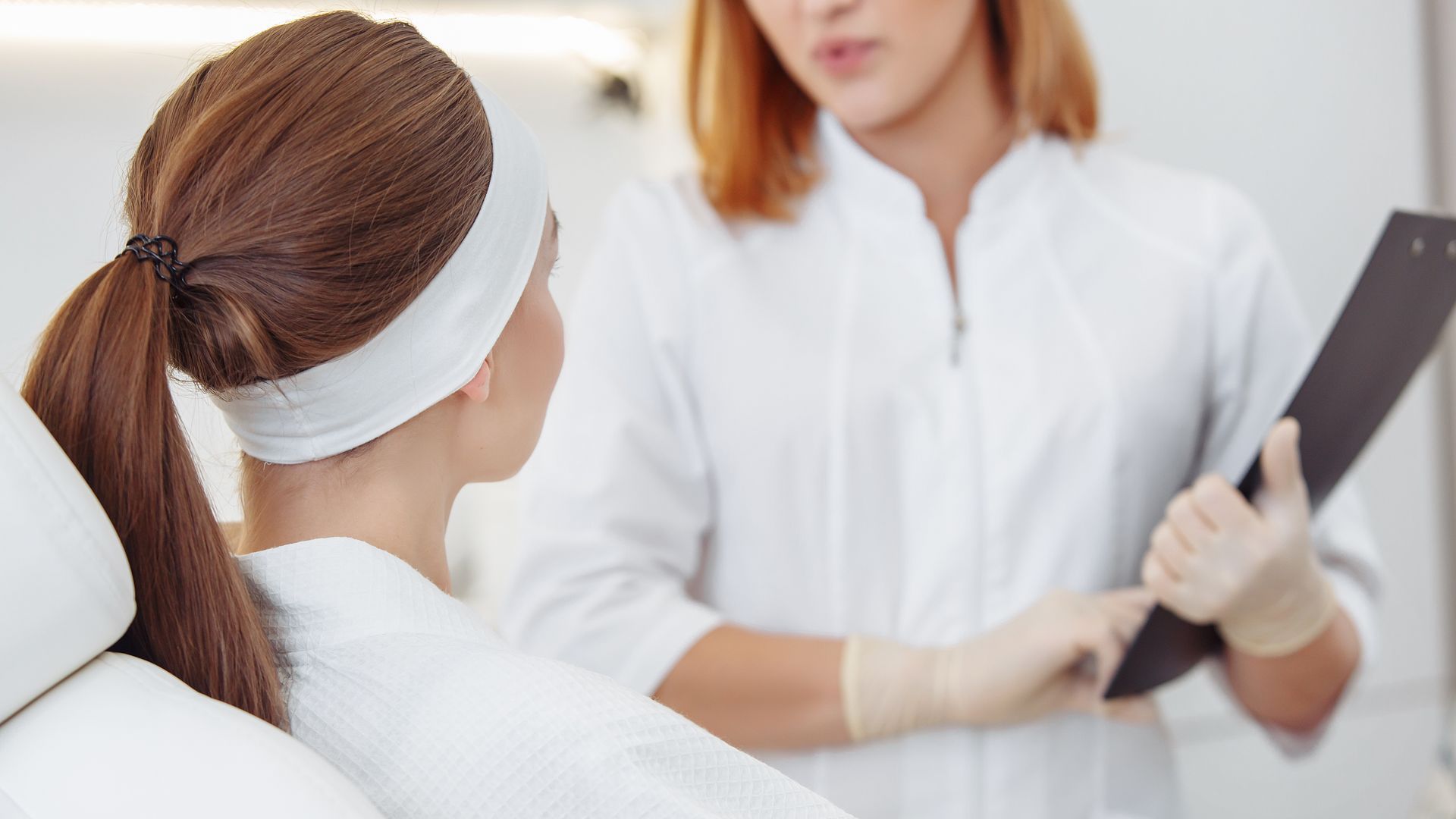 Patient talking with clinician in a white office, holding a black folder.