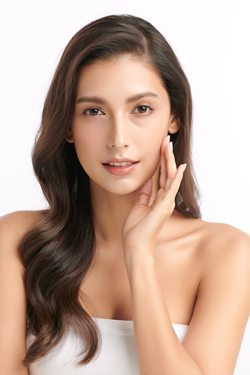 Portrait of a woman with long dark hair touching her face against a white background